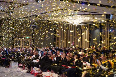 confetti poppers fill the room as the emcee congratulates the graduates on their achievements.