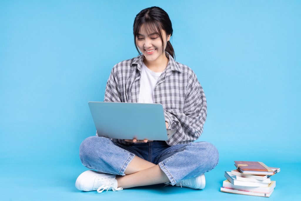 A student studying on her laptop while sitting cross legged on the floor.