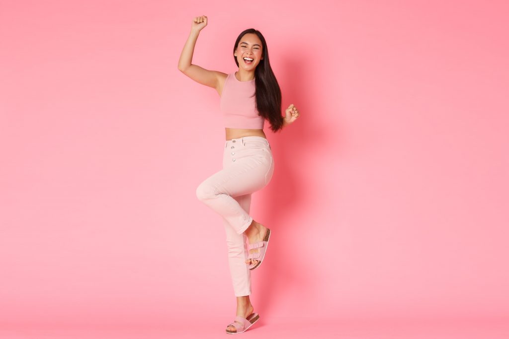Asian lady cheering and smiling with her hands joisted in the air.