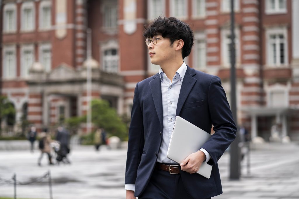 Male asian business student in formal wear carrying a laptop.