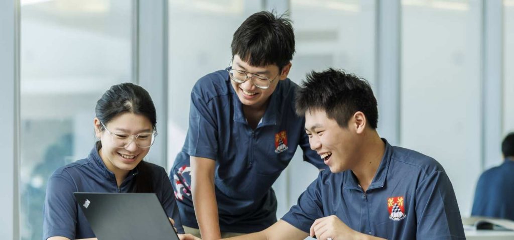 Group of MDIS college students smiling while looking at a computer screen.