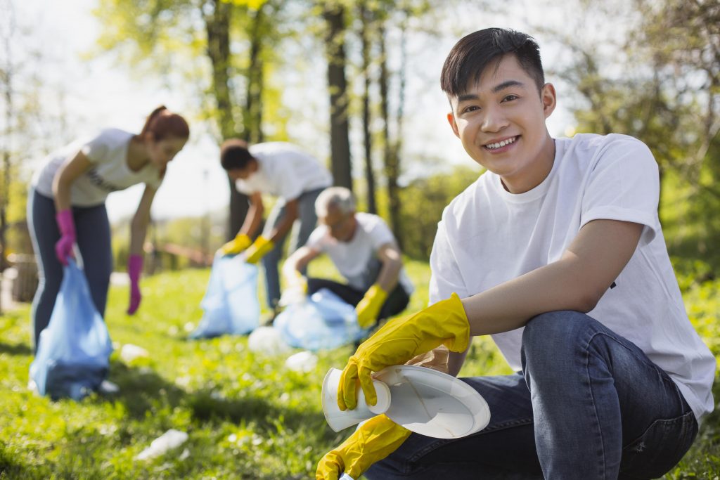 A young Asian student participating in volunteer work by picking up trash at the park.