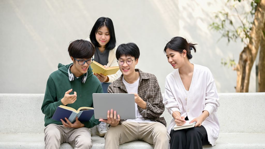 A group of students studying together using their books and laptop in an outdoor setting.