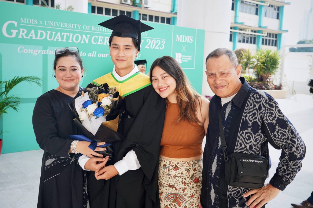 An MDIS Graduate posing with his family at the MDIS- University of Roehampton London Graduation Ceremony's photo wall.