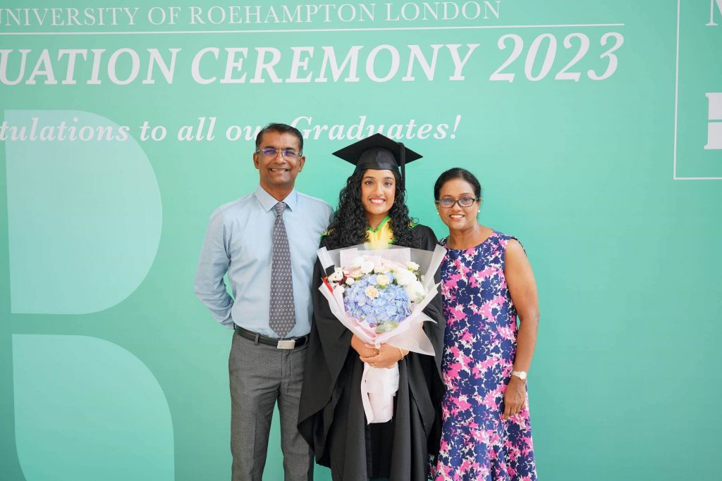 An MDIS Graduate posing with her parents at the MDIS- University of Roehampton London Graduation Ceremony's photo wall. 