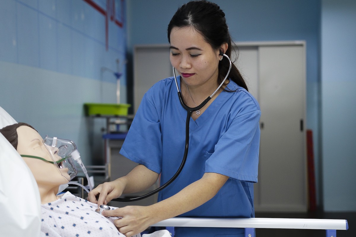 An MDIS Nursing student practicing her skills on a dummy patient.