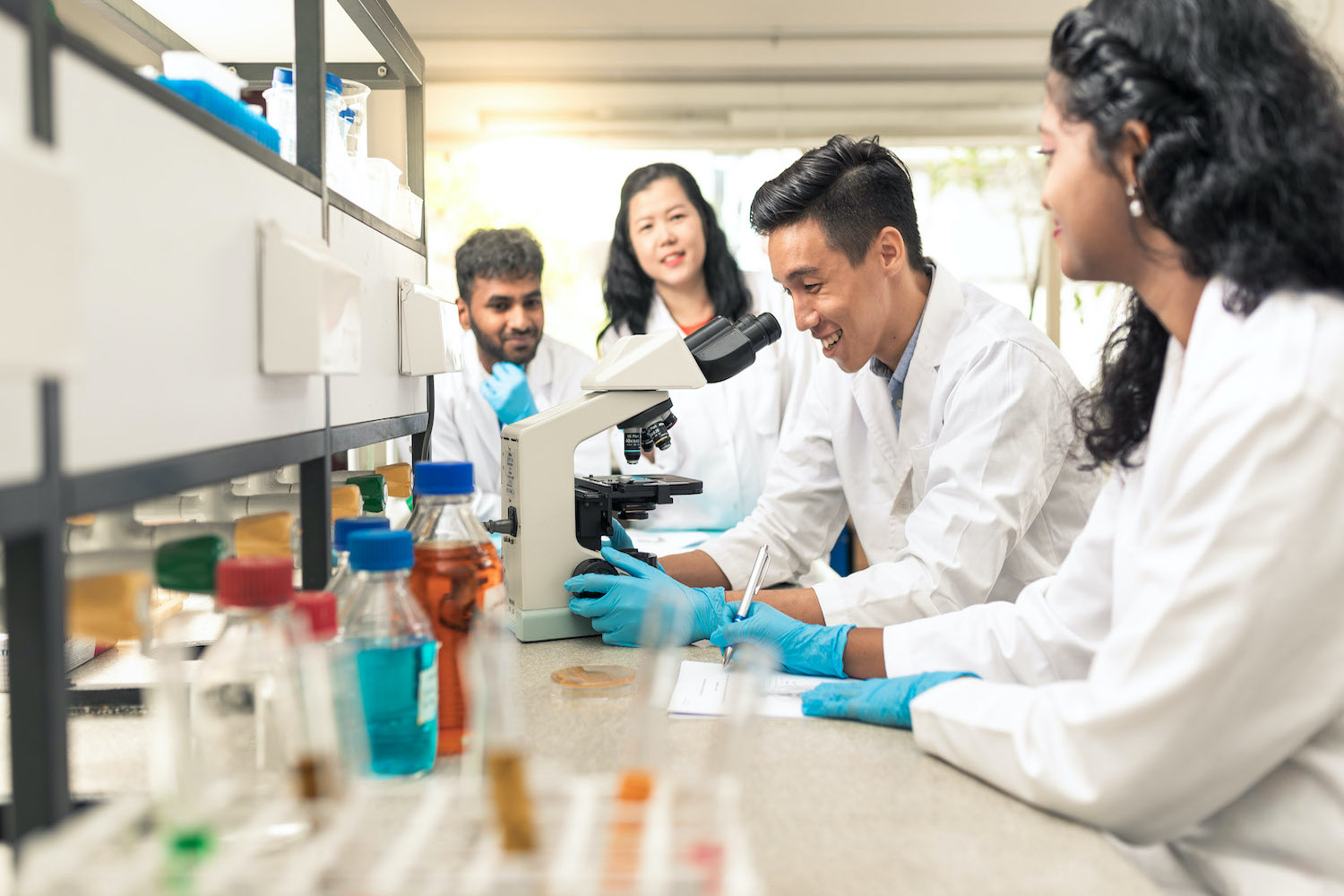 A group of life science students waiting for the results of a study through a microscope.