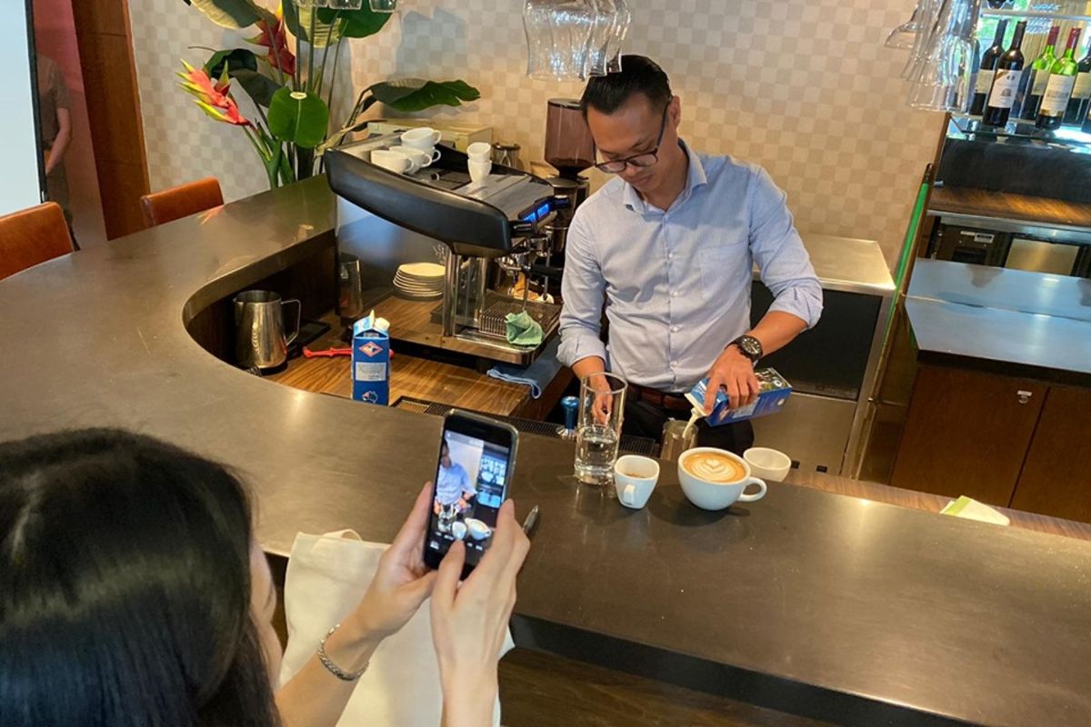 An MDIS student being filmed while making coffee art.